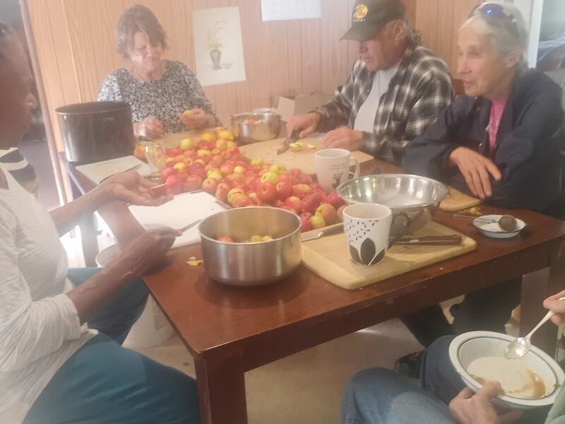 Members gathered around a kitchen table sorting and cutting a harvest of tomatoes.